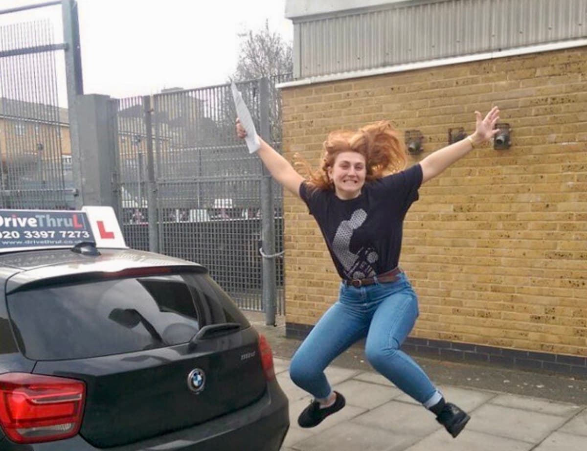 Student jumping for joy on pass day with DriveThruL car